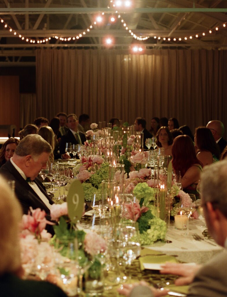 Looking down an endless wedding banquet table illuminated by hundreds of glass cylinder candles and overhead bistro lights.