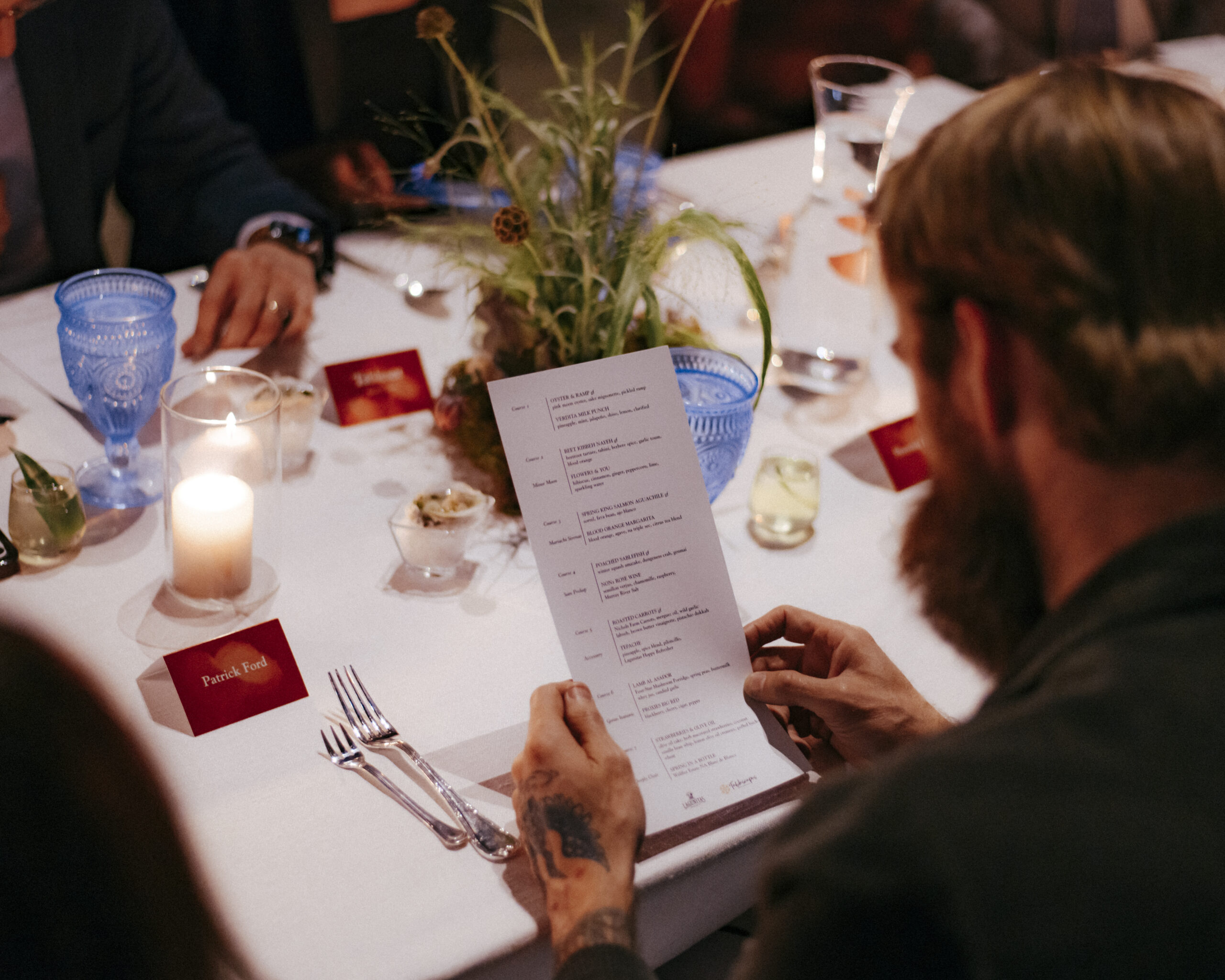 party-hosting-essentials.jpgGuest reading a multi-course menu at a table set with blue glass goblets and pillar candles.