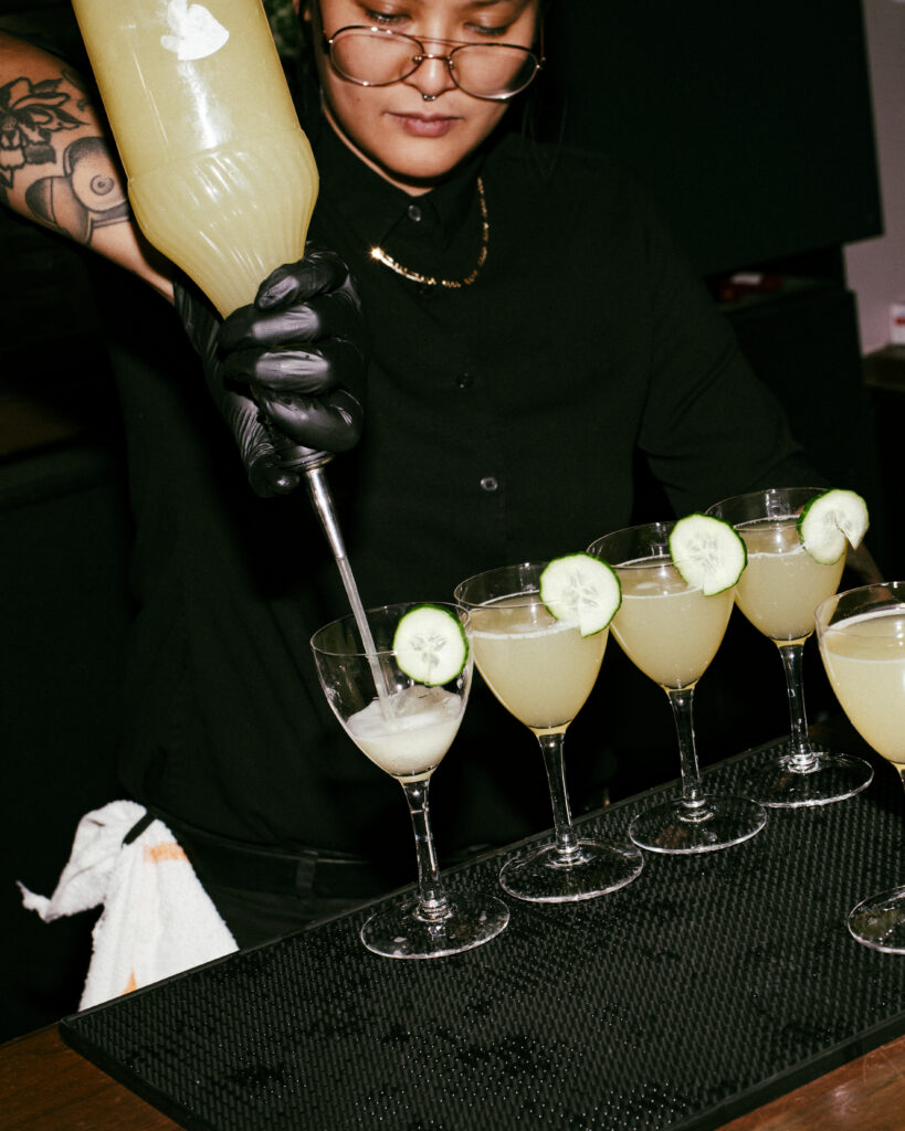 Bartender pouring fresh cucumber-garnished cocktails on a bar mat for a high-end Chicago dinner party. 