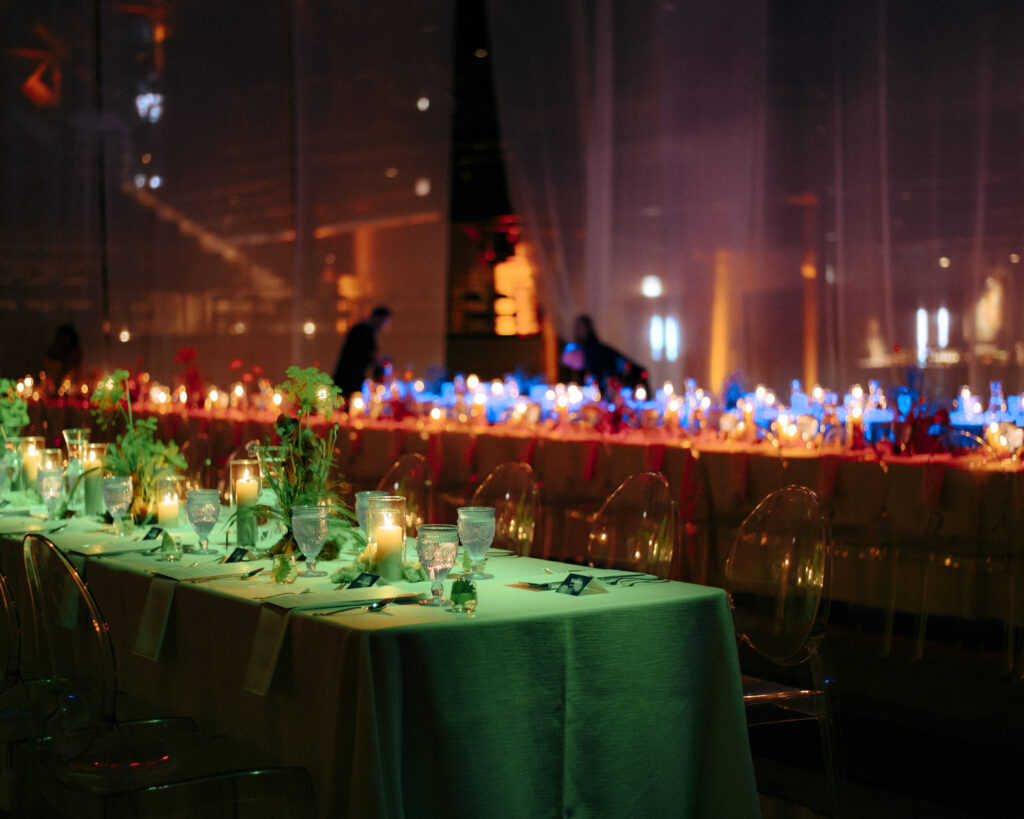 Long dinner tables glowing under vibrant green and amber mood lighting inside the Salt Shed. 