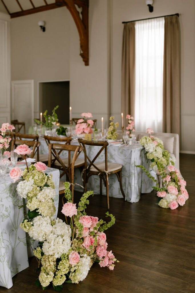Looking down a long banquet table styled with garden style wedding decor, wood cross-back chairs, and tall candles.