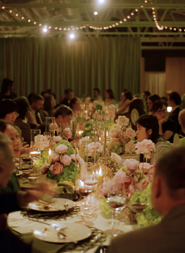 Warmly lit, atmospheric view of an indoor wedding reception at Sarabande with long family-style dinner tables.