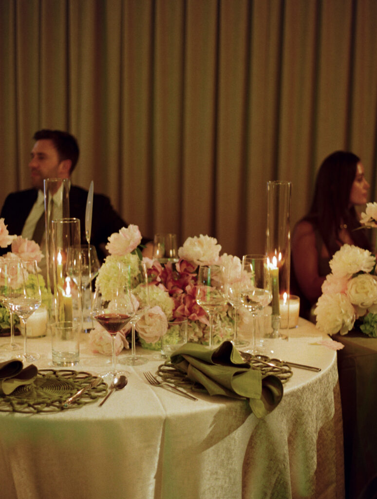 Elegant round wedding table layout at Sarabande Chicago featuring sage napkins, glass cylinders, and white velvet linens.