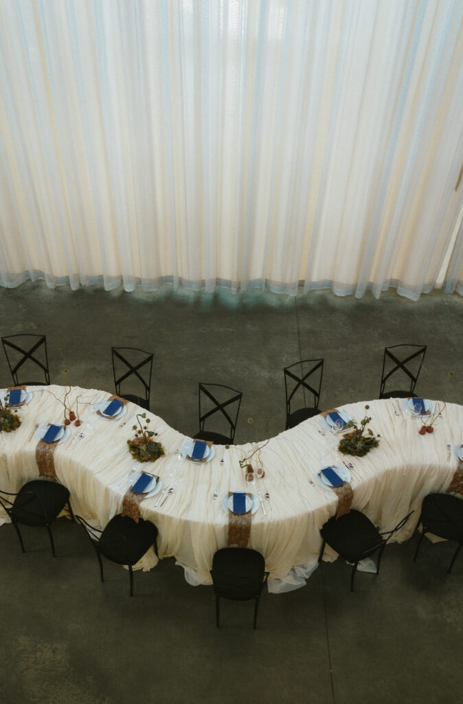 Closer overhead look at gathered maize linens and navy napkins on a winding serpentine wedding table layout.