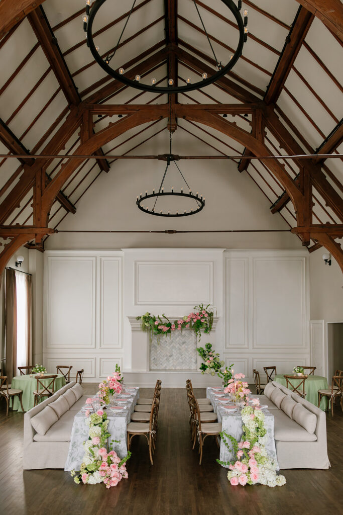 Wide shot of a symmetrical wedding reception floor plan featuring central banquet tables with linen couches inside a timber-framed chapel.