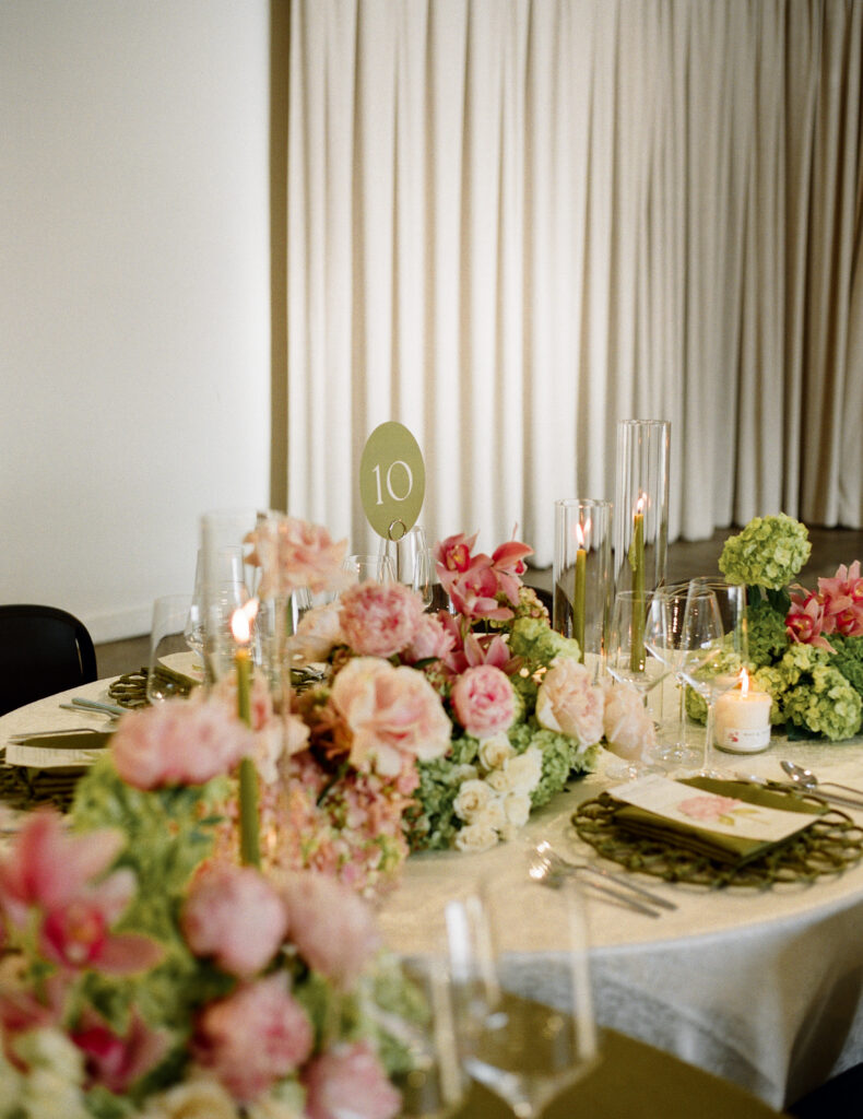 Close-up of an elegant wedding table setting with olive green accents, green taper candles in glass cylinders, and clear wine glasses.