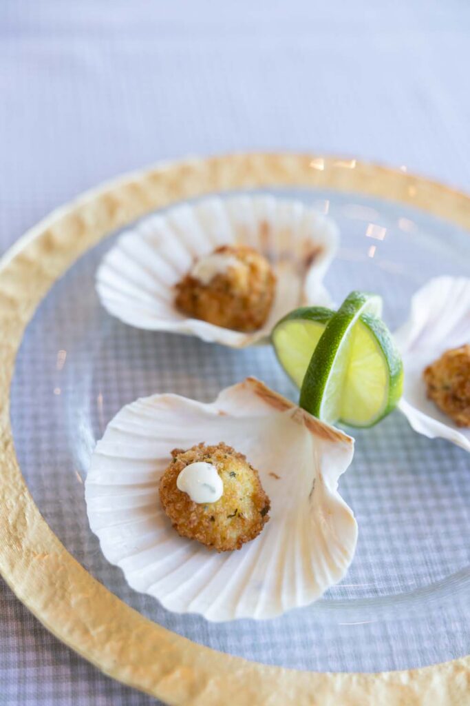 Seared scallops presented on natural baking shells on a gold charger plate.