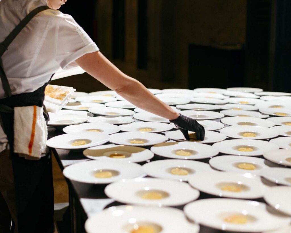 Catering staff plating individual small bites into white belly button bowls.