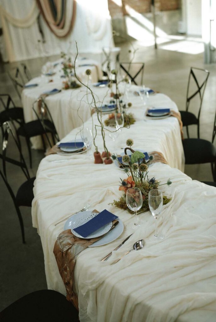 Long serpentine dining table setup with white linens, blue accents, and black chairs.