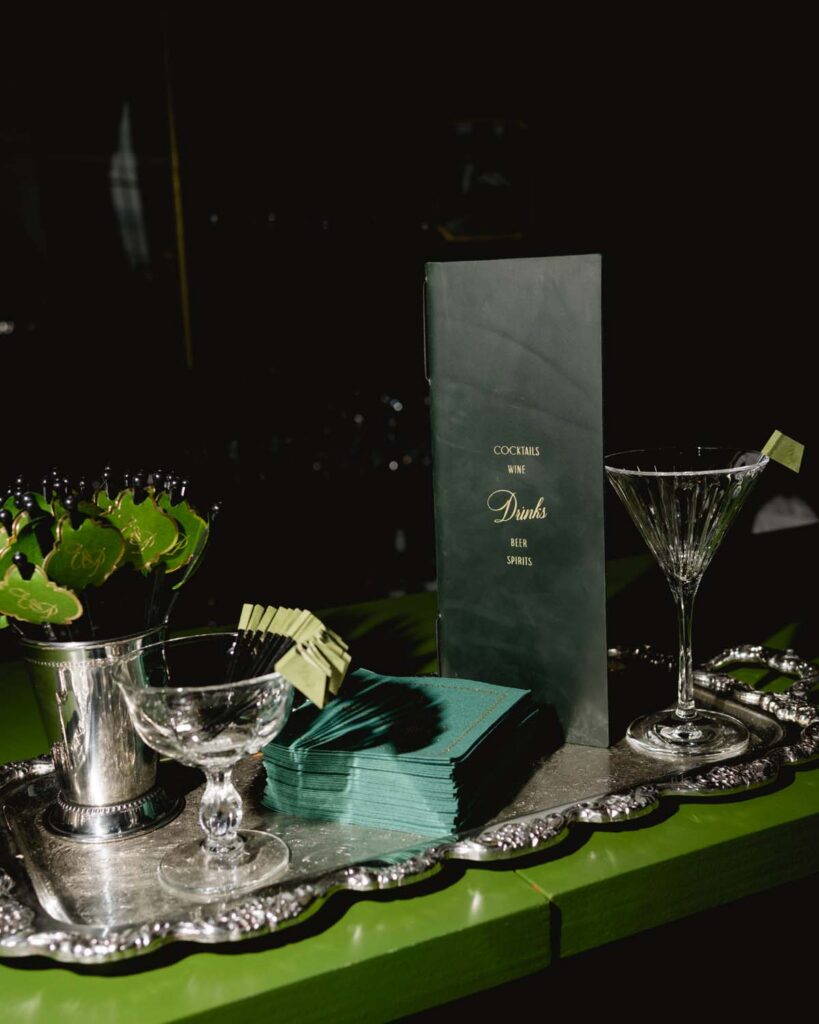 Vintage silver tray with clear ball martini glass and cocktail garnish picks on a green bar top.