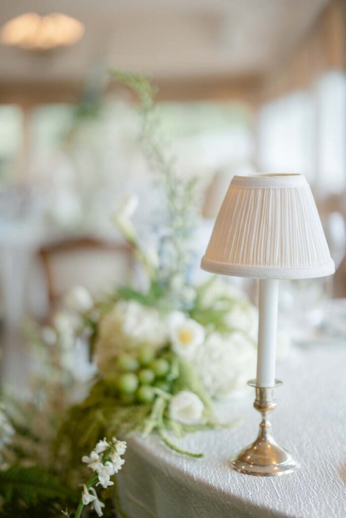 Petite white shade tabletop lamp on a silver candleholder base on a wedding dining table.