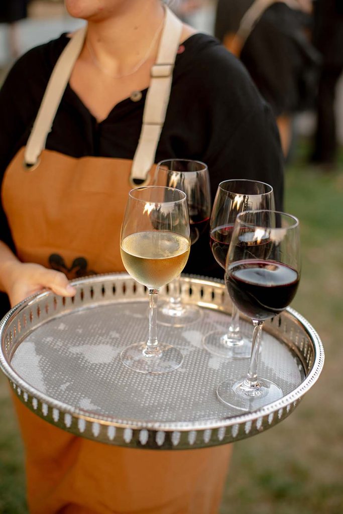 Catering staff member holding a polished silver tray with wine glasses filled with red and white wine for butler service.