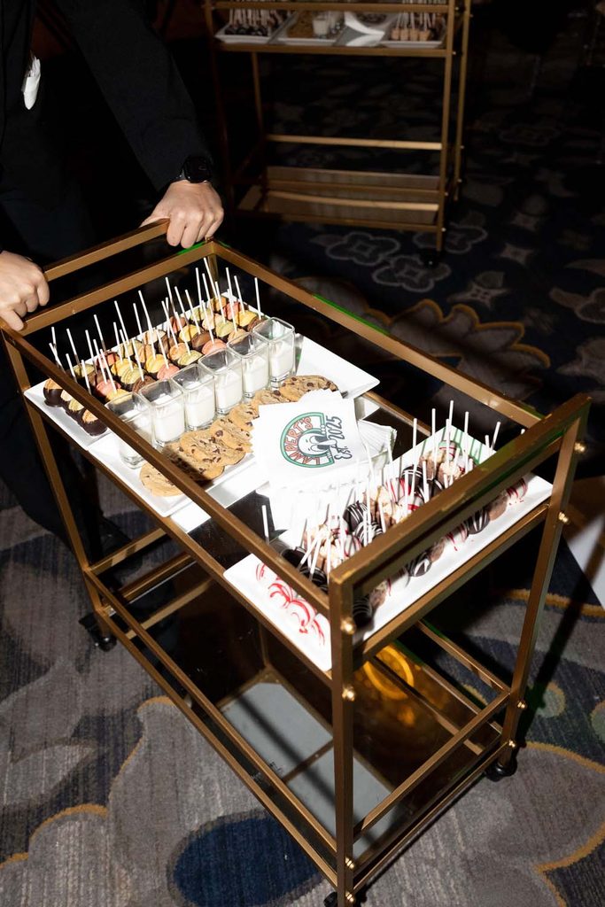 Server pushing a two-tiered gold bar cart loaded with mini dessert shooters, cookies, and sweet treats on passed platters.
