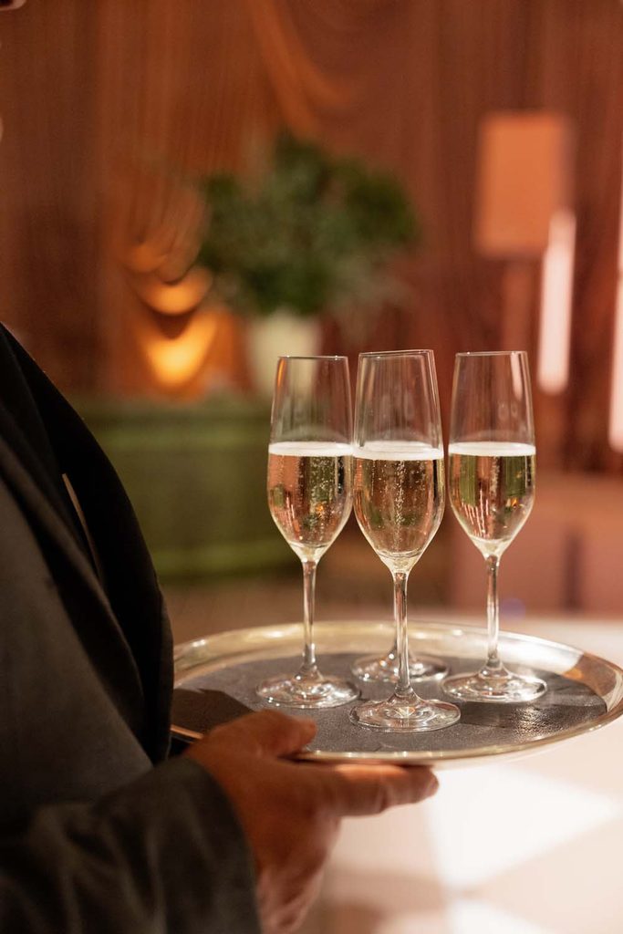 Butler-passed champagne flutes filled with sparkling wine on a silver tray at an elegant event.
