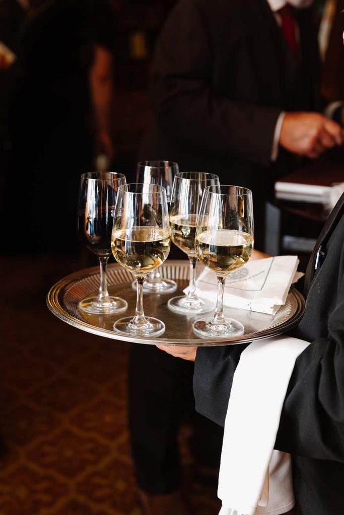 Server holding a silver tray with glasses of red and white wine during a catered cocktail reception.